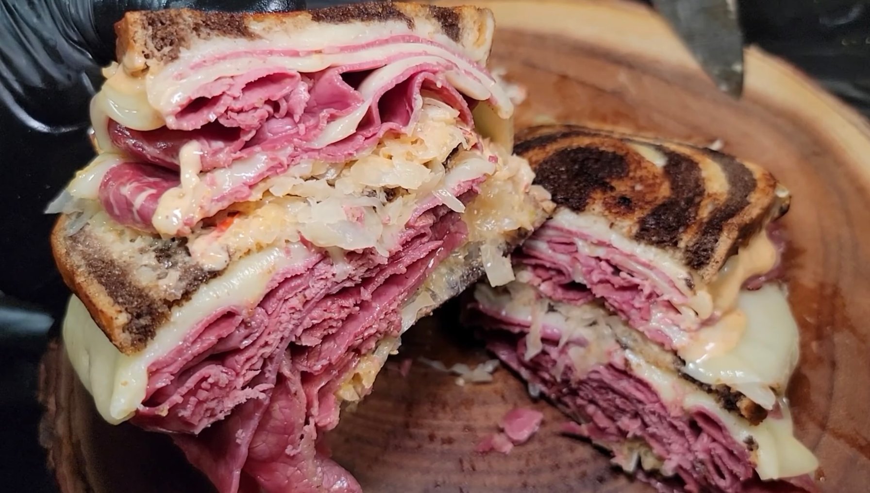 Classic Reuben sandwich on rye bread with corned beef, melted Swiss cheese, sauerkraut, and Russian dressing, served with pickles.